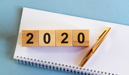 Year 2020 sign text number on wooden cube blocks on a white notebook planner and golden pen on blue table desk. 2020 recap summary review concept