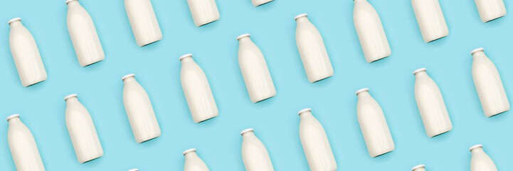 Pattern made with transparent glass bottle of milk on blue background. Flat lay Top view Banner