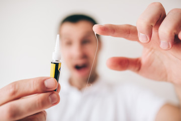 Young man isolated over white background. Guy hold instant glue in hand and touching it. Scream and yell during process. Blurred defocused man.