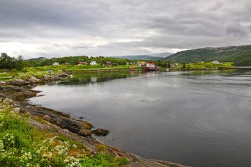 Fototapeta na wymiar Beautiful landscape along with waters edge with a village, church & mountains in the background, Saltstraumen, Municipality of Bodo, Nordland county, Norway.