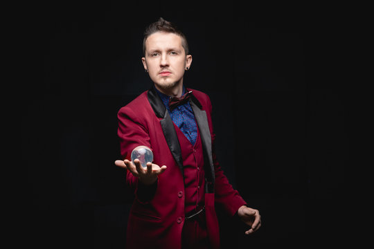 Illusionist magician shows levitation trick with ball in hands on black background