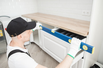 Kitchen installation, worker fixing door assembling furniture white carved cabinet front