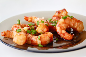 Large pacific shrimps in sweet and sour sauce with chopped green onions on a glass plate.