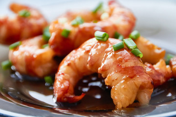 Large pacific prawns in spicy chili sauce with chopped green onions on a glass plate.