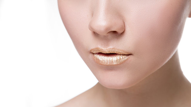 Gold Paint drips from the lips, golden liquid drops on beautiful model girl's mouth, gold metallic paint smudges make-up. Beauty woman face makeup close up.