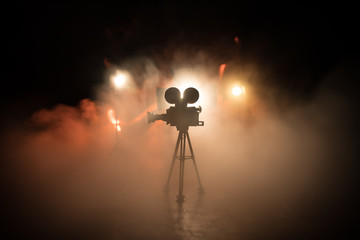 Movie concept. Miniature movie set on dark toned background with fog and empty space. Silhouette of vintage camera on tripod. - obrazy, fototapety, plakaty