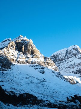 Snowy white peaks of the Rocky Mountains on the Icefield Parkway hit by a the sunset light with blue sky.
