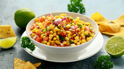 Mexican Corn Salsa in white bowl with lime and tortilla chips. Healthy food