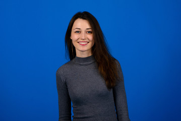 Photo of smiling, cheerful young female in grey dress on blue background