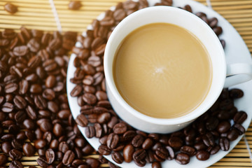 White ceramic cup of hot coffee and beans on Woven mat with natural light morning in the garden. Caffeine drinks cause a fresh feeling. Top view