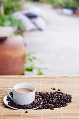 White ceramic cup of hot coffee and beans on Woven mat with natural light morning in the garden. Caffeine drinks cause a fresh feeling.