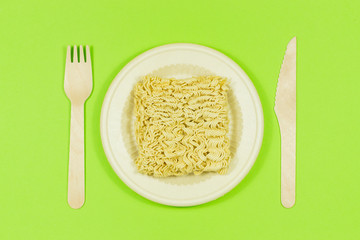 Instant pasta on a colored background with disposable wooden eco cutlery.