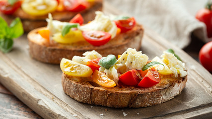 Tomato bruschetta and mozzarella cheese with basil on a rustic wooden board