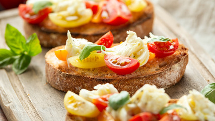 Tomato bruschetta and mozzarella cheese with basil on a rustic wooden board