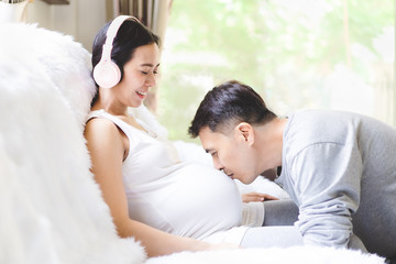 Asian husband is kiss his beautiful pregnant wife with love and they smiling together with happiness moment, concept of love, relation, expectation and  parenthood in  family lifestyle.