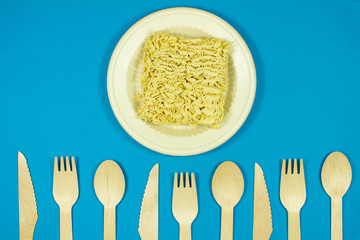 Instant pasta on a colored background with disposable wooden eco cutlery.