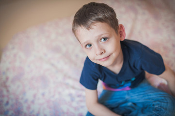 The happy boy sits on the bed. View from above, child looks at the camera. close-up.