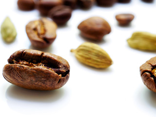 Coffee beans and cardamom grains are scattered on a white glossy surface. Shallow depth of field and highly blurred background. Copy space. 