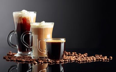 Espresso, latte macchiato and Irish coffee on black reflective background with coffee beans.