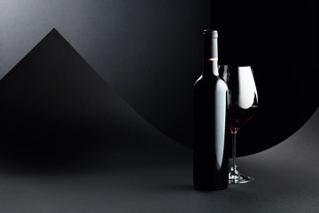 Bottle and glass of red wine on a dark background.