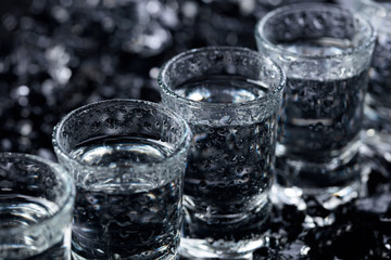 Damp glasses of vodka with ice on a black reflective background.