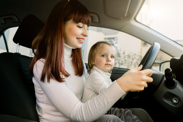 Mother with little baby girl sitting in front seat and driving car together. Child in danger, no...
