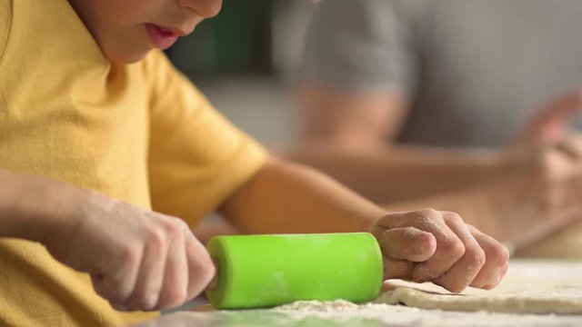 Children cooks pizza. Boy and girl having fun with father. Prepering ingredients for pizza. Roll out the dough with a rolling pin