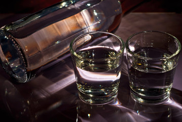 Glasses with alcohol near the bottle. Transparent drink on a purple background.