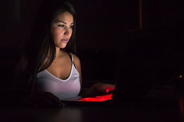 Beautiful latina gaming girl plays game on gaming notebook PC in dark area