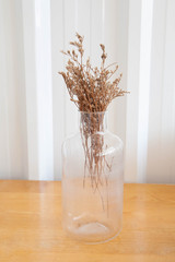 Small bouquet of dry flowers in glass vase on wooden table. Minimalism and vintage concept.