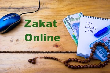 Texts zakat online (alms-giving) on wooden table during covid-19 lockdown. Conceptual.Obligation to aid the poors. Calculator, mouse and note book with texts on white. Selective focus.