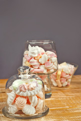 Sweets in a glass on a wooden table. Transparent utensils with marshmallows and biz on a shabby old board. Pink with white soft candies. Sweets on a purple background.