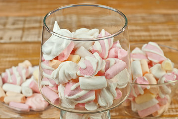 Sweets in a glass on a wooden table. Transparent utensils with marshmallows and biz on a shabby old...