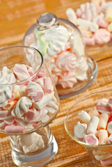Sweets in a glass on a wooden table. Transparent utensils with marshmallows and biz on a shabby old board. Pink with white soft candies close up.
