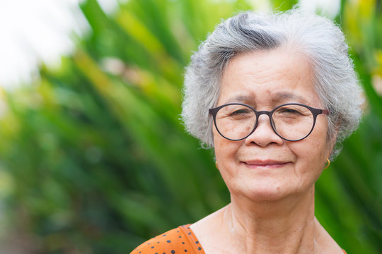 Portrait of an elderly woman wearing eyeglasses, smiling and looking at the camera while standing in a garden. Space for text. Concept of old people and healthcare