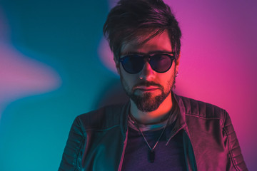 Ragazzo italiano guardando in camera, con occhiali da sole, in studio, in discoteca, con luci rosse e blu, con barba e capelli, in posa da modello