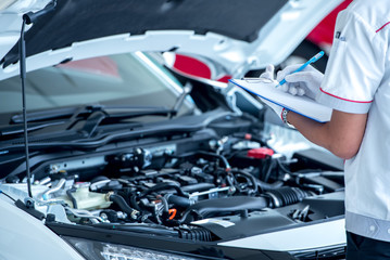 Asian engineers or technicians are checking and recording car data into notes. Asian mechanic staff checked the car engine oil in the car repair shop on the list.