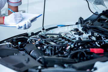 Asian engineers or technicians are checking and recording car data into notes. Asian mechanic staff checked the car engine oil in the car repair shop on the list.