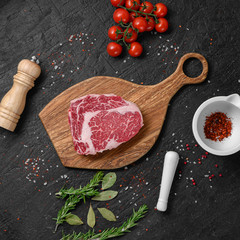 Raw ribeye beef steak on wooden board with rosemary