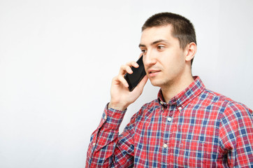 Young man in a plaid shirt with a smartphone on a white background. The guy holds a smartphone by...