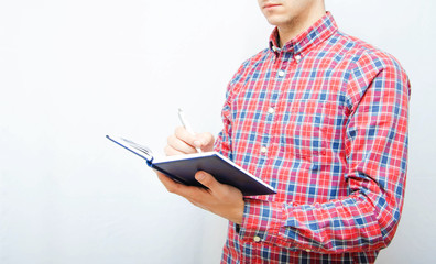 Young man in a plaid shirt with a smartphone on a white background. The guy holds a notebook and writes information, tasks,  reminders