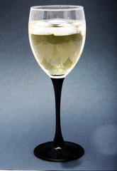 A glass of white wine with pieces, ice cubes. Wine with ice on a black background. Glass with a black  leg