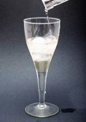 A glass of white wine with pieces, ice cubes. Wine with ice on a black background. Wine flows from the neck of the bottle. A stream of white  wine