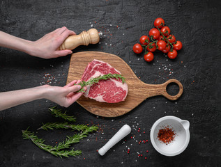 Rib eye raw marbled meat steak on a dark background with female hands
