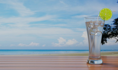 Lemon juice in tall clear glass and ice with straws on the table, wood texture There is a backdrop to the sea and the beach. 3D Rendering