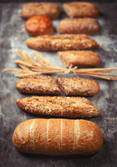 Fresh bakery food. Crusty loaves of mixed breads and buns and ears of wheat on rustic table background. Shallow DOF and copy space for your advertising text message