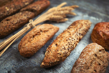 Fresh bakery food. Crusty loaves of mixed breads and buns and ears of wheat on rustic table background. Shallow DOF and copy space for your advertising text message