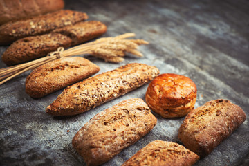 Fresh bakery food. Crusty loaves of mixed breads and buns and ears of wheat on rustic table background. Shallow DOF and copy space for your advertising text message