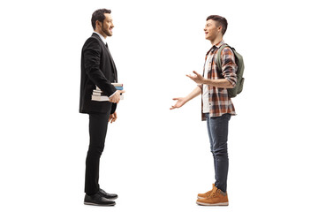 Full length profile shot of a man in a black suit holding books and talking with a male student