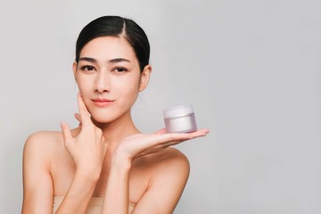 Young beautiful asian woman with clean, fresh and bright skin,holding Cream jar with positive emotional,isolated on gray background,Beauty Cosmetics and Facial treatment Concept